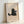 May include: Framed poster print leaning against white wall showing a cute black cat illustration holding a light blue mug with marshmallows, with "Meow" text below. Simple minimalist art style with beige textured background in natural wood frame.