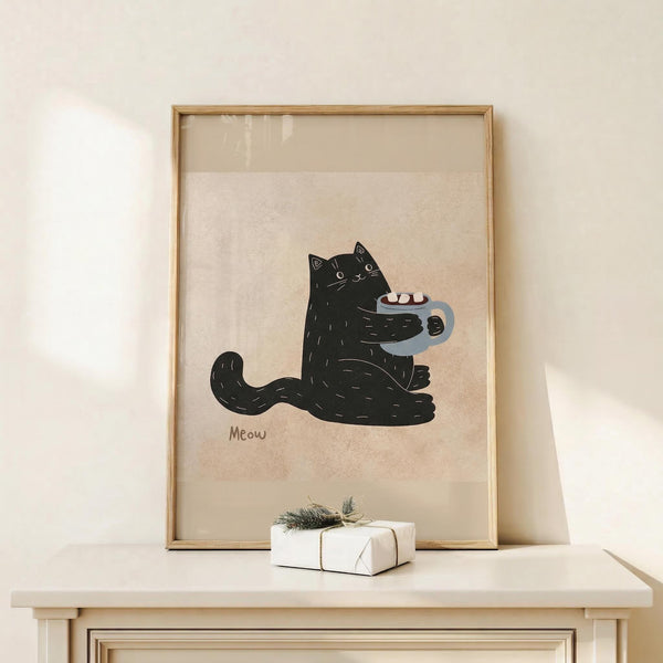 May include: Framed artwork showing a black cat sitting upright holding a gray mug with marshmallows, with "Meow" text below on cream textured paper background. Natural wood frame displayed on light wooden surface next to small white gift box with twine and greenery sprig against neutral beige wall.