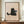 May include: Framed poster print featuring a simple black cat illustration holding a light blue mug with marshmallows, with "Meow" text below on beige textured background. Brown wooden frame displayed on walnut credenza beside white ceramic vase and stacked books in neutral-toned room with white paneled walls.