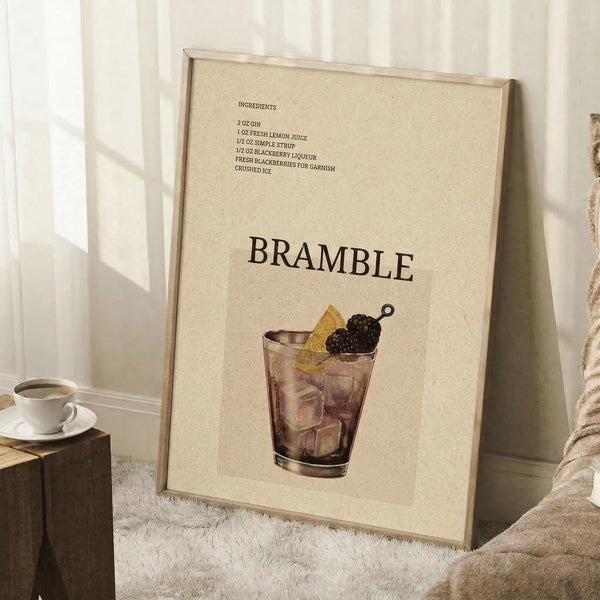 May include: Framed beige poster with illustrated bramble cocktail recipe displayed in cozy living room setting with white walls, wooden stool holding coffee cup, textured rug, and neutral furniture. Artwork shows dark cocktail glass with blackberry garnish and ingredient list in brown text against cream background.