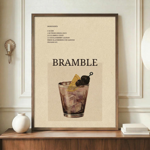May include: Framed vintage-style cocktail recipe poster displaying a Bramble drink illustration with ingredients list, shown in brown wooden frame on wooden credenza beside white ceramic vase and books against cream paneled wall with decorative brass sconce