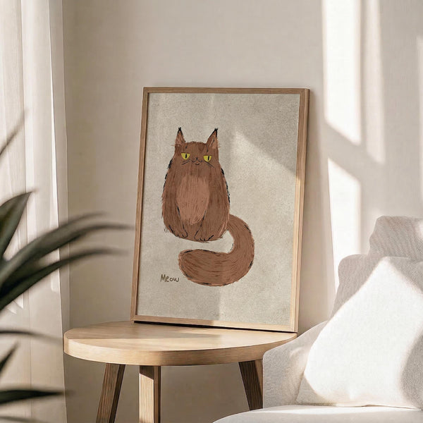 May include: Framed poster print featuring a fluffy brown cat with bright yellow-green eyes and long bushy tail, sitting upright with "Meow" text below. The artwork has a hand-drawn watercolor style on cream textured background in a thin wooden frame. Displayed on a round light wood side table next to a beige upholstered chair and plant leaves, with natural sunlight streaming across neutral walls.