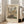 May include: Framed museum poster print leaning against white wall next to beige sectional sofa in bright living room. The vintage-style artwork shows a busy European street scene with Gothic cathedral towers, colorful buildings, and crowds of people. Cream matting surrounds the impressionist painting reproduction in light wood frame on hardwood floors with area rug.