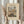 May include: Hands holding a framed art print featuring Camille Pissarro's painting of a bustling French street scene with Gothic cathedral towers, market crowds, and colorful buildings. The beige matted print shows "The MET museum" and "Grocery Street, Rouen" text. Dried pampas grass visible on left side against neutral curtained background.