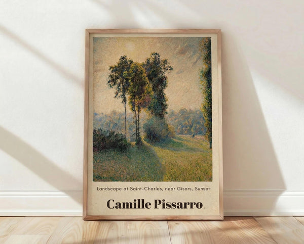 May include: Framed art print displaying an impressionist landscape painting with tall trees along a winding country path, rendered in soft greens, yellows and blues with a hazy sunset sky. The wooden frame rests against a white wall on light wooden flooring, with natural window light casting diagonal shadows across the scene.