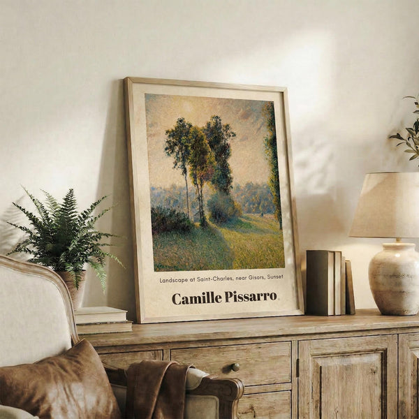 May include: Framed Impressionist landscape poster featuring tall trees in a pastoral setting with warm golden and green tones, displayed on a rustic wooden sideboard alongside potted fern, ceramic vase, and books in a cozy living room with beige chair and neutral walls.
