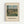 May include: Framed art print showing Camille Pissarro's impressionist landscape painting of rural French countryside with rolling green fields, farm buildings with red-tiled roofs, tall poplar trees, and cloudy blue sky. The print features cream matting in a light wood frame, mounted on a white wall. The painting depicts pastoral farmland with small figures working in the fields and a winding path through the valley.