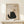 May include: Framed poster displaying a black fluffy cat with golden eyes sitting beneath a dangling yarn ball, with "Meow" text below. Artwork has textured beige background in natural wood frame, displayed on light wooden console table alongside small wrapped gift with dried botanicals against cream wall.