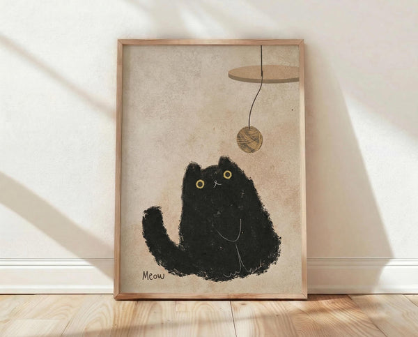 May include: Framed poster print leaning against white textured wall on light wood floor. Artwork shows black textured cat silhouette with golden eyes looking up at brown yarn ball dangling from curved string. Background has cream vintage paper texture. Word "Meow" appears in bottom left corner. Natural wood frame with warm lighting and soft shadows across scene.