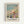 May include: Framed poster print featuring a Claude Monet beach scene with people in period dress enjoying a sunny day by turquoise waters. Shows figures with parasols and hats scattered across sandy beach with cliffs in background. Includes Monet's signature and quote about painting like a bird sings. Light wood frame against white wall, soft impressionist brushstrokes in pastels and blues.