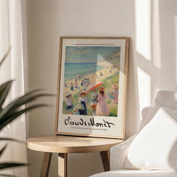 May include: Framed art print of an impressionist beach scene with people under colorful umbrellas on sandy coastline. Print features Claude Monet signature and quote below the artwork. Wooden frame sits on round wooden side table next to beige upholstered chair. Soft natural lighting creates shadows on white wall. Green plant leaves visible in corner.