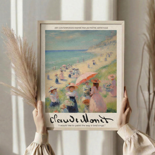 May include: Person holding framed art print featuring impressionist beach scene with figures in period dress, parasols, and coastal landscape in soft pastels. Print shows Claude Monet signature and quote below artwork. Person wears cream sweater, holds dried wheat stems, neutral interior background with curtains visible.
