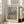 May include: Framed art print showing Monet's impressionist painting of Venice's San Giorgio Maggiore church with distinctive domes across shimmering water, with wooden posts in foreground. Print has cream matting with "CLAUDE MONET" and "EXHIBITION ART" text, displayed in light wood frame leaning against white wall next to beige upholstered chair in bright, naturally-lit room with white wooden floors.