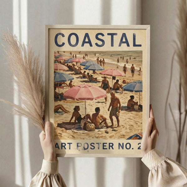 May include: Hands holding a framed vintage-style beach scene poster showing people with colorful pink and blue umbrellas on sandy shore. Wood frame against neutral curtained background with dried pampas grass visible on left side. Warm, natural lighting creates soft shadows.