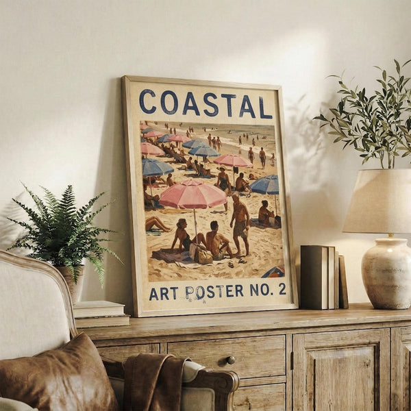 May include: Framed vintage-style beach scene poster displayed on rustic wooden sideboard in neutral-toned living room. Artwork shows people with colorful umbrellas on sandy beach in warm, muted tones. Scene includes fern plant, ceramic vase with olive branches, stacked books, and cream upholstered chair with leather throw blanket. Natural lighting creates soft shadows on white textured wall.