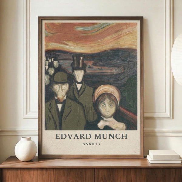 May include: Framed reproduction of Munch's "Anxiety" painting showing three pale figures with haunting expressions against a swirling orange and dark blue sky. The poster has cream matting in a thin brown frame, displayed on a wooden credenza beside a white ceramic vase and stacked books against beige walls with white trim.