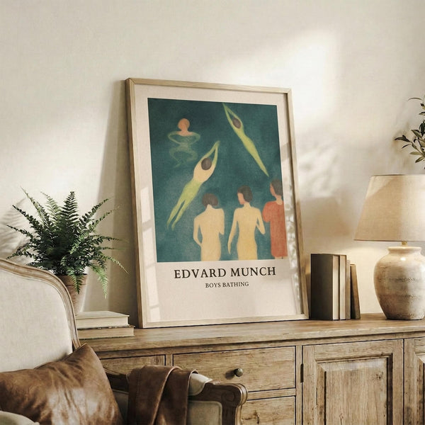 May include: Framed art print displayed on rustic wooden sideboard in neutral living room. Print shows stylized figures in teal and cream tones with text below. Scene includes fern plant, stacked books, ceramic vase, brown leather chair, and soft natural lighting creating cozy home decor atmosphere.