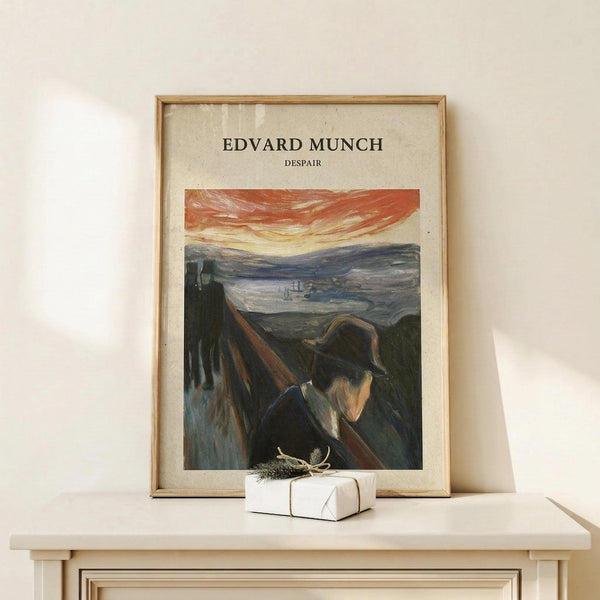 May include: Framed art print featuring Edvard Munch's expressionist painting showing a figure in dark clothing and hat against a dramatic landscape with orange-red sky and winding path. The vintage-style poster has cream background with black text at top. Displayed on light wood surface with small wrapped gift box, natural lighting creating soft shadows on white wall.