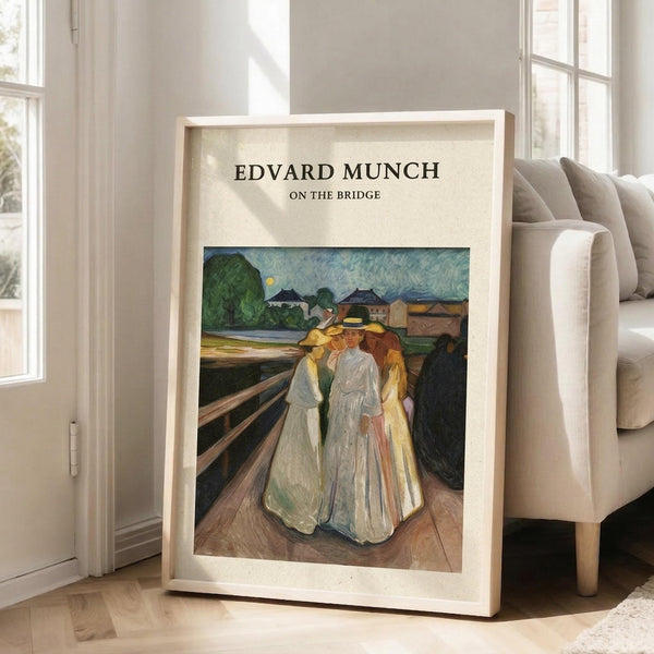 May include: Framed art print displaying Edvard Munch's painting of three figures in flowing white and yellow dresses standing on a wooden bridge, with green landscape and buildings in background, positioned on light wood floor against white wall next to beige upholstered sofa in bright, naturally-lit room with large windows