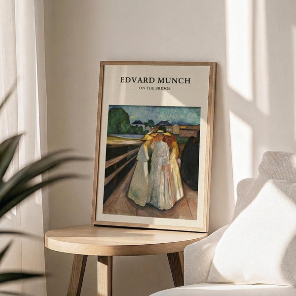 May include: Framed art print featuring Edvard Munch's expressionist painting of three figures in flowing white and yellow robes standing on a wooden bridge, displayed on a round wooden side table next to a beige upholstered chair with plant shadows cast on cream walls from natural sunlight.