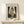 May include: Framed poster print of Edvard Munch's "The Kiss" artwork showing two embracing figures in black and white sketch style, displayed in light wood frame on white wooden console table with small wrapped gift box beside it against cream wall