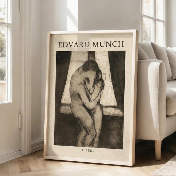 May include: Framed art print featuring Edvard Munch's "The Kiss" - a black and white etching showing two nude figures embracing by a window. The artwork displays expressive, sketchy linework characteristic of Munch's style. Positioned against white walls in a bright living room with beige upholstered chair, large windows, and natural lighting creating soft shadows on hardwood floors.