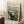 May include: Framed art print of Munch's The Scream displayed in a cozy living room corner. The black and white expressionist artwork shows a figure with hands to face on a bridge with swirling sky lines. Cream-colored mat in light wood frame, leaning against white wall near beige textured rug, wooden side table with white coffee cup, and neutral fabric furniture.