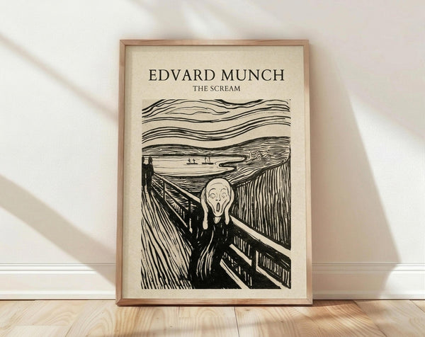 May include: Black and white reproduction of Edvard Munch's famous expressionist artwork showing a figure with hands to face in a screaming pose on a bridge, with swirling dramatic sky lines. Framed in light wood frame with cream matting, leaning against white wall on light wooden floor with soft natural lighting casting shadows.