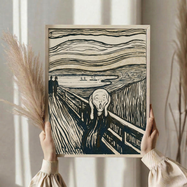 May include: Person holding framed reproduction of famous expressionist artwork showing figure with hands to face in screaming pose on wooden bridge. Black and white woodcut print style with dramatic wavy sky lines. Light wooden frame, neutral wall background, dried pampas grass visible to left. Hands wearing cream colored ruffled sleeves grip frame edges.