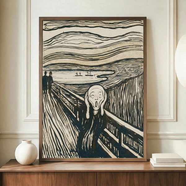 May include: Black and white reproduction of an expressionist artwork showing a figure with hands to face in an anguished scream on a bridge, with two people in background and swirling sky above. The print is displayed in a brown wooden frame on a wooden sideboard next to a white ceramic vase and stack of books in a room with cream walls and white trim.
