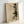 May include: Framed abstract artwork featuring botanical pine branch silhouettes and geometric line drawings including a partial circle, displayed in light wood frame against white wall. The print has an aged, vintage appearance with cream and sepia tones, combining natural plant imagery with minimalist architectural sketches in a collage-style composition.