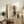 May include: Framed abstract artwork featuring a zen circle and pine tree silhouette in muted beige and black tones, displayed on a rustic wooden console table alongside decorative pottery, books, and a fern plant in a neutral-toned living room setting with warm natural lighting.