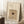 May include: Framed beige poster displaying espresso martini cocktail recipe with ingredients list including vodka, coffee liqueur, simple syrup and espresso. Shows martini glass with coffee beans floating on foam. Wooden frame leaning against white wall on textured white rug, next to wooden block with white coffee cup and beige throw blanket.