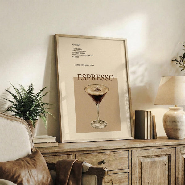 May include: Framed espresso martini cocktail recipe poster with vintage-style illustration of martini glass topped with coffee beans, displayed on rustic wooden sideboard alongside leather chair, potted fern, ceramic vase, and stacked books in warm neutral-toned living room setting.