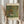 May include: Person holding framed art print featuring Gustav Klimt's colorful garden painting with sunflowers, wildflowers, and lush greenery in vibrant yellows, reds, purples, and greens. Light wood frame with cream matting displays museum attribution text. Dried wheat stems visible alongside, soft neutral clothing and curtained window background create warm, natural styling.