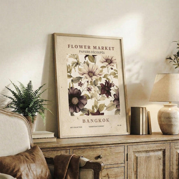 May include: Framed botanical poster with vintage-style floral design featuring purple and cream flowers with green foliage, displayed on rustic wooden sideboard alongside fern plant, ceramic vase, and stacked books in neutral-toned living room setting with beige armchair and throw pillows.