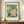 May include: Framed botanical poster with white flowers and yellow centers against green foliage background, displayed on wooden sideboard next to white ceramic vase and books in elegant room with cream walls and white molding