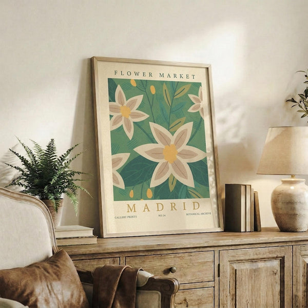 May include: Framed botanical poster with white flowers on green background displayed on rustic wooden console table alongside fern plant, books, ceramic vase and table lamp in neutral-toned living room setting with beige armchair