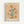 A framed vintage-style botanical poster featuring stylized flowers in warm earth tones including orange, yellow, pink, and teal against a cream background. The artwork shows daisy-like blooms on green stems with scattered leaves and small botanical elements throughout. Text reads "FLOWER MARKET" at top and "NEW YORK" at bottom with "GALLERY PRINTS NO.5 MUSEUM OF MODERN ART" in smaller text. The print is displayed in a light wood frame against a white wall.
