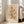 May include: Framed botanical poster with vintage cream background featuring illustrated orange and yellow flowers, teal green stems and leaves, scattered small botanical elements. Text reads "Flower Market" at top and "New York" at bottom. Light wood frame leans against white wall next to beige sofa in bright, airy living room with large windows and natural lighting.