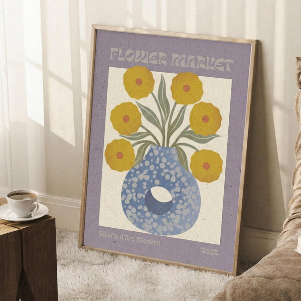 May include: Framed vintage-style poster with purple border featuring yellow flowers in a blue polka-dotted vase, leaning against white wall corner next to wooden side table with coffee cup and beige throw blanket on textured rug.