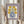 May include: Hands holding a framed vintage-style poster featuring yellow flowers in a blue polka-dotted vase against a cream background with purple border. The poster reads "Flower Market" at top and "Galerie d'Art Moderne No.35" at bottom. Person wears a beige ruffled sleeve top and holds dried pampas grass, photographed against white curtained window background.