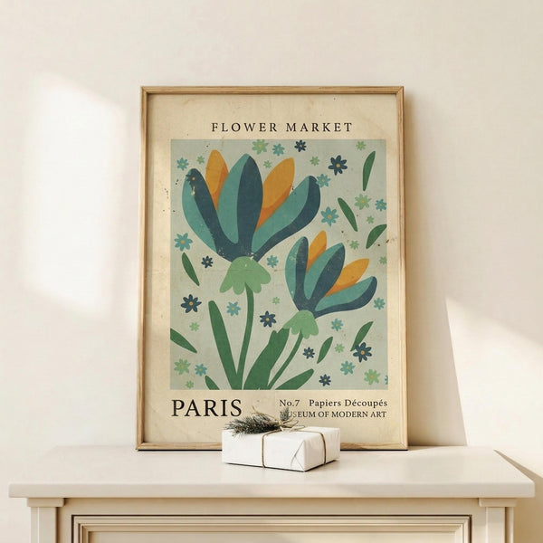 May include: Framed vintage-style botanical poster with stylized blue, teal, and orange flowers on pale green background, displayed on light wood console table next to small wrapped gift with twine and greenery sprig against cream wall
