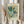May include: Hands holding a framed vintage-style botanical poster featuring two stylized flowers with teal, orange, and green petals surrounded by small decorative blooms. The aged cream-colored print reads "Flower Market Paris" and "Museum of Modern Art" with dried pampas grass visible beside it against soft natural lighting.