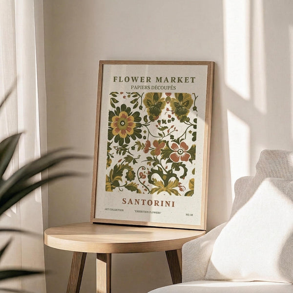 May include: Framed vintage botanical poster with ornate floral pattern in green, brown and cream tones displayed on round wooden side table next to beige upholstered chair. Natural sunlight streams across neutral wall creating soft shadows. Live plant visible in corner of minimalist room setting.