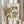 May include: A person in cream clothing holding a framed botanical poster featuring vintage-style flowers in green, yellow, and coral tones with "FLOWER MARKET" and "SANTORINI" text. The scene shows dried pampas grass beside them against soft white curtains in natural lighting.