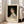 May include: Framed art print leaning against white wall beside beige sofa in bright living room. The poster features a classical portrait painting of a young woman with curly brown hair wearing a white dress against dark background. Exhibition-style layout with cream background and black text reading "PIERRE AUGUSTE exhibition" and "Gabrielle Cot" with "Pierre Auguste's Daughter" below. Light wood frame, hardwood floors.