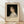 May include: Framed vintage-style exhibition poster featuring a classical portrait painting of a young woman with curly dark hair in a white dress against black background. The cream-colored poster displays "PIERRE AUGUSTE exhibition" text below the artwork. Wooden frame leans against white wall on light wood flooring with natural shadows.