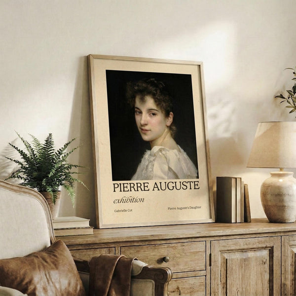 May include: Framed vintage-style art print featuring a classical portrait of a young woman with curly dark hair wearing a white dress against a black background. The poster displays "PIERRE AUGUSTE exhibition" text below the portrait. Shown in a light wood frame on a rustic wooden sideboard alongside books, a ceramic vase, fern plant, and table lamp in a neutral-toned living room setting.
