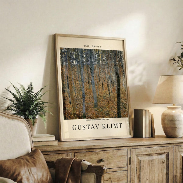 May include: Framed art print of autumn forest with tall beech trees in golden and brown tones, displayed on rustic wooden sideboard alongside fern plant, ceramic vase, stacked books, and leather chair in warm, naturally-lit living room setting